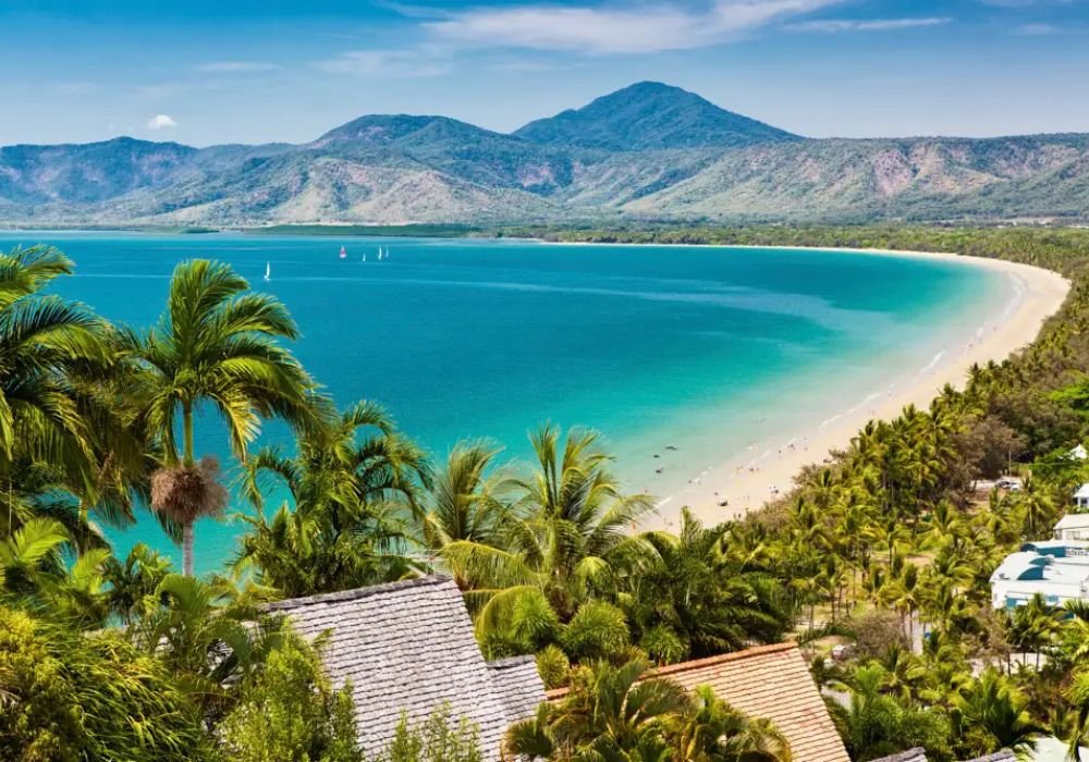 A panoramic view of Four Mile Beach near Cairns, with turquoise waters, palm trees, and mountains in the background